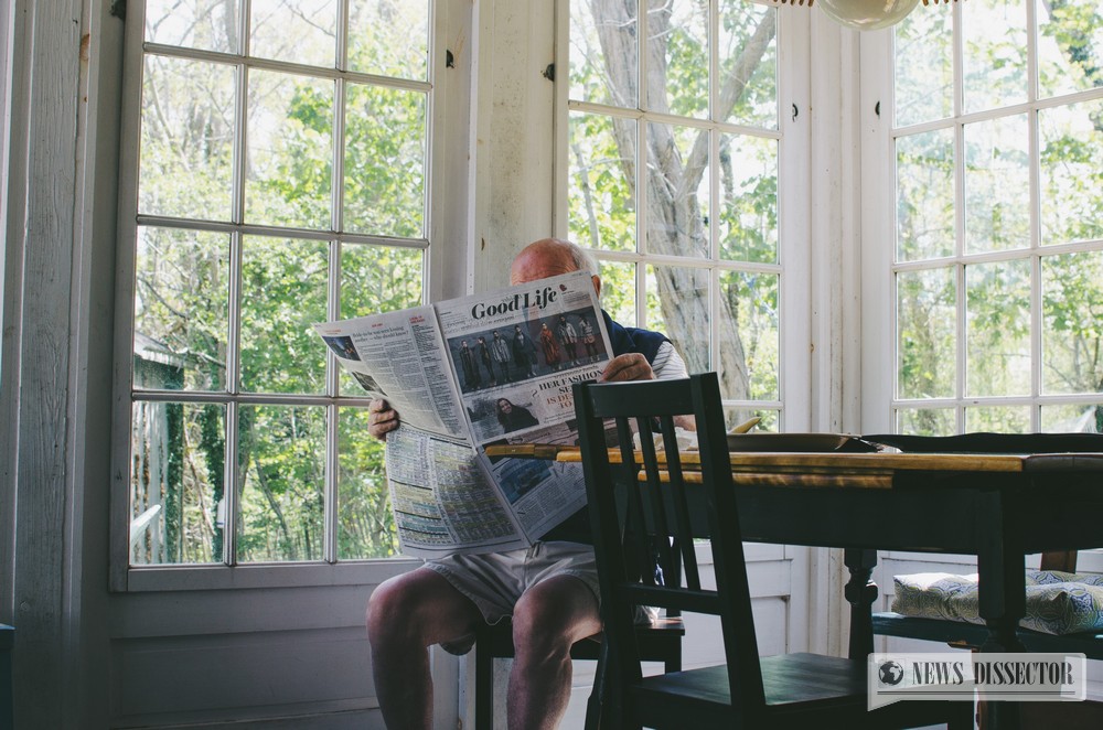 Old man reading a newspaper in his own home