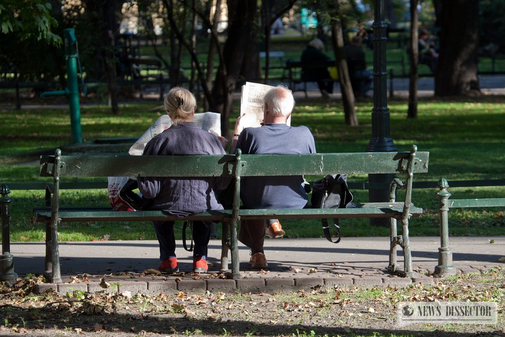 People reading the newspaper on a bench