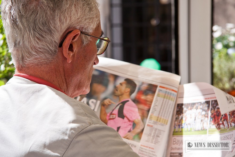 An old man reading the sports section of a tabloid